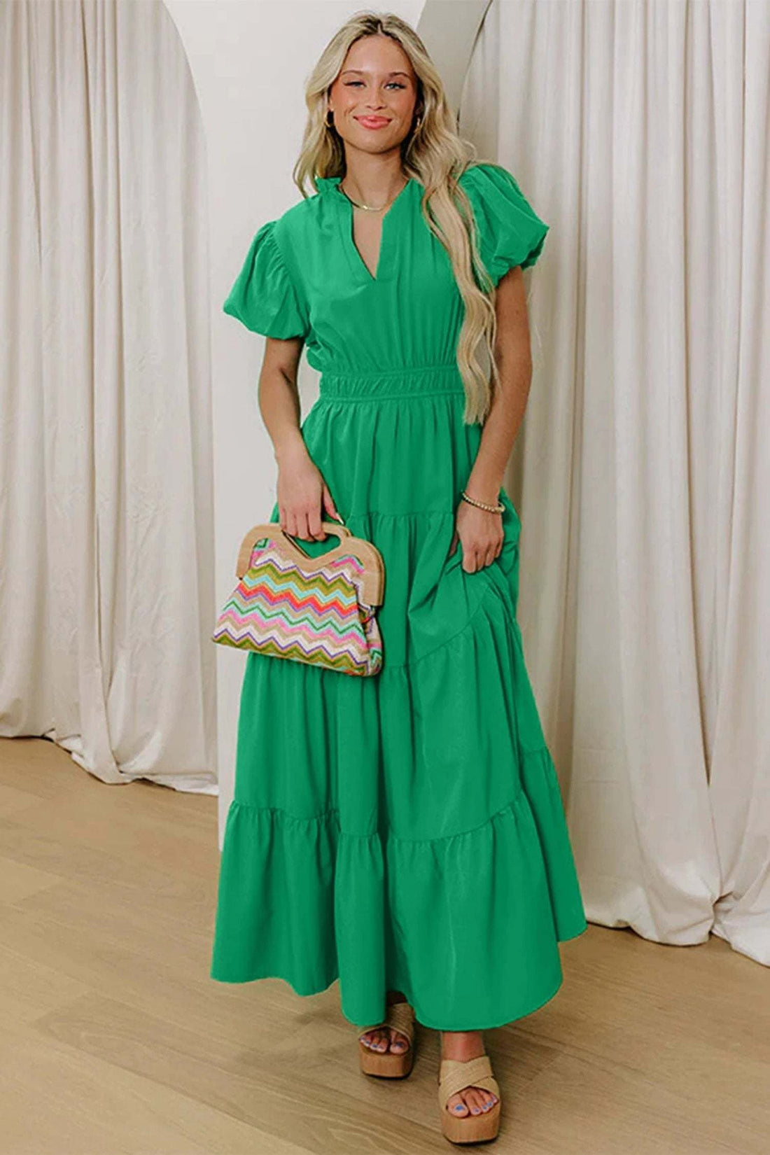 Green puff-sleeve maxi dress with a cinched waist, worn by a model holding a colorful chevron handbag.