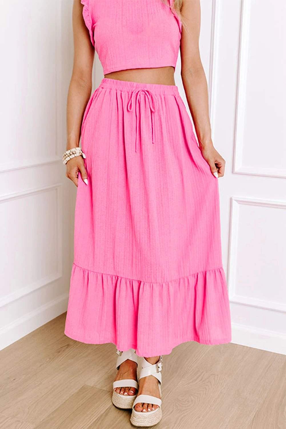 Woman wearing vibrant pink Boho Glow textured ruffle crop vest and lace-up maxi skirt set