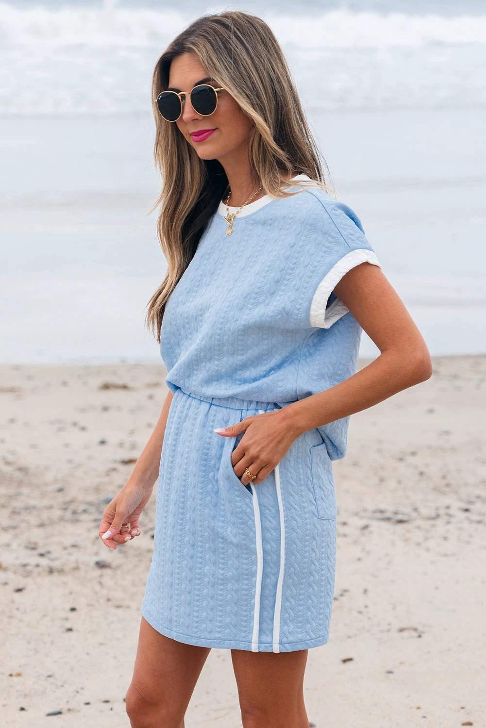 Woman wearing a soft blue textured crewneck tee with contrast white trim paired with a pocketed skirt featuring a clean side stripe