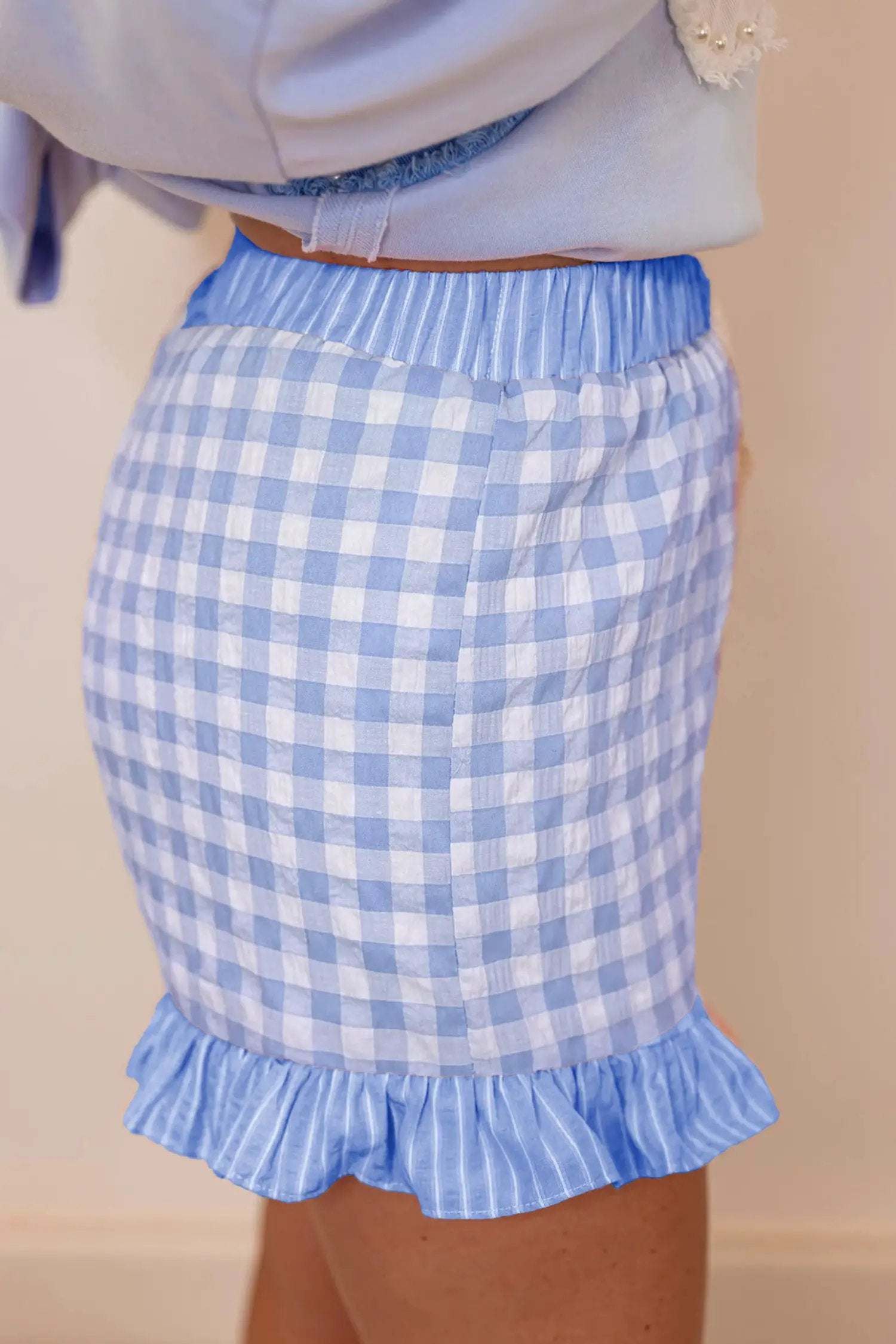 Woman wearing gingham ruffle hem shorts with lace tie waist detail outdoors