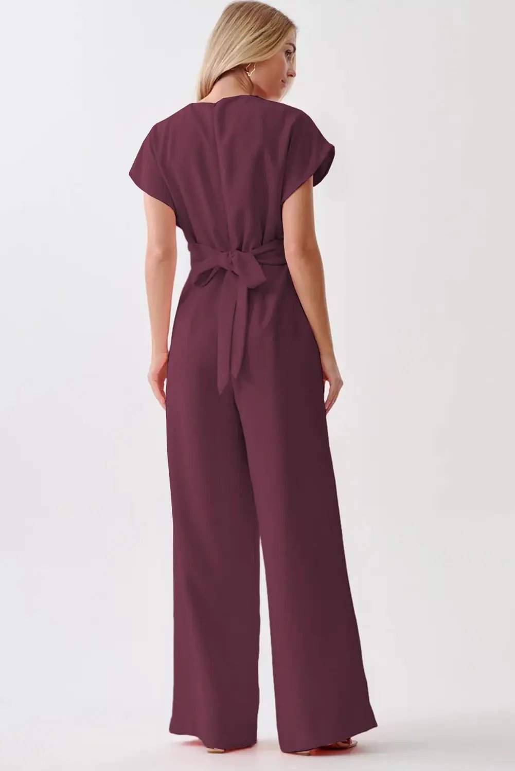 Woman wearing a wine-colored knot-waist cap sleeve jumpsuit with wide-leg silhouette
