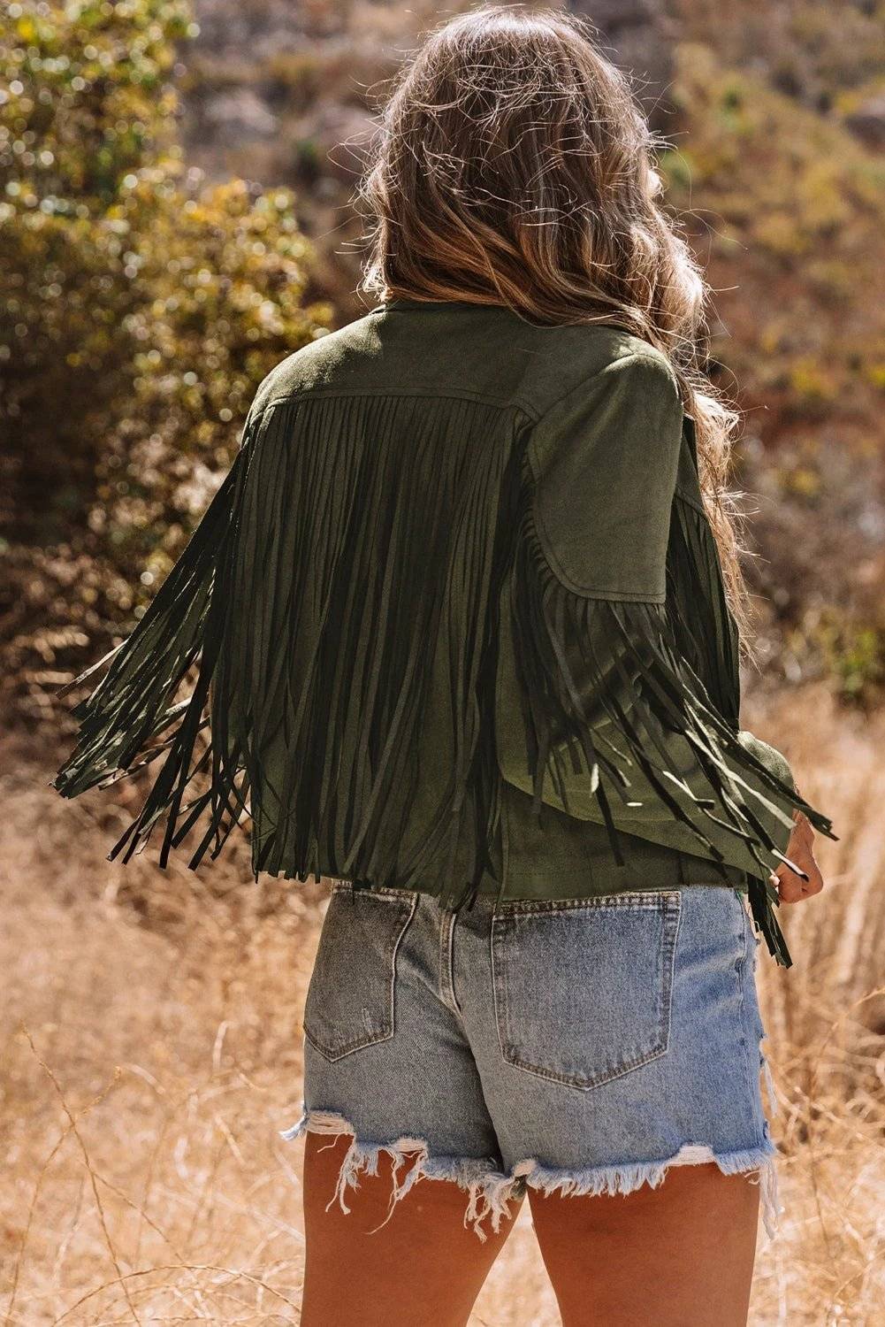 Woman wearing a cropped faux suede Western fringe jacket with sleeve fringe and western detailing.