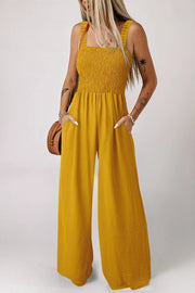 Woman wearing a ginger smocked sleeveless wide-leg jumpsuit with pockets outdoors