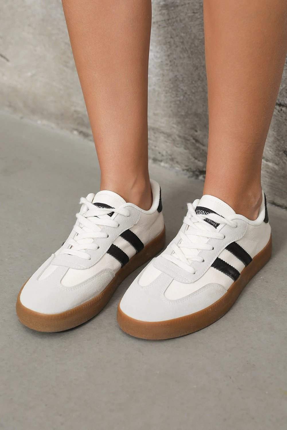 White striped lace-up flat sneakers with black accents and gum sole showcasing chic mom energy style
