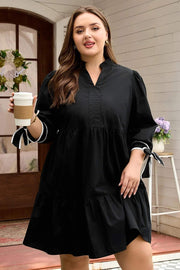 Plus size black V-neck mini dress with contrast trim and knot cuffs on model