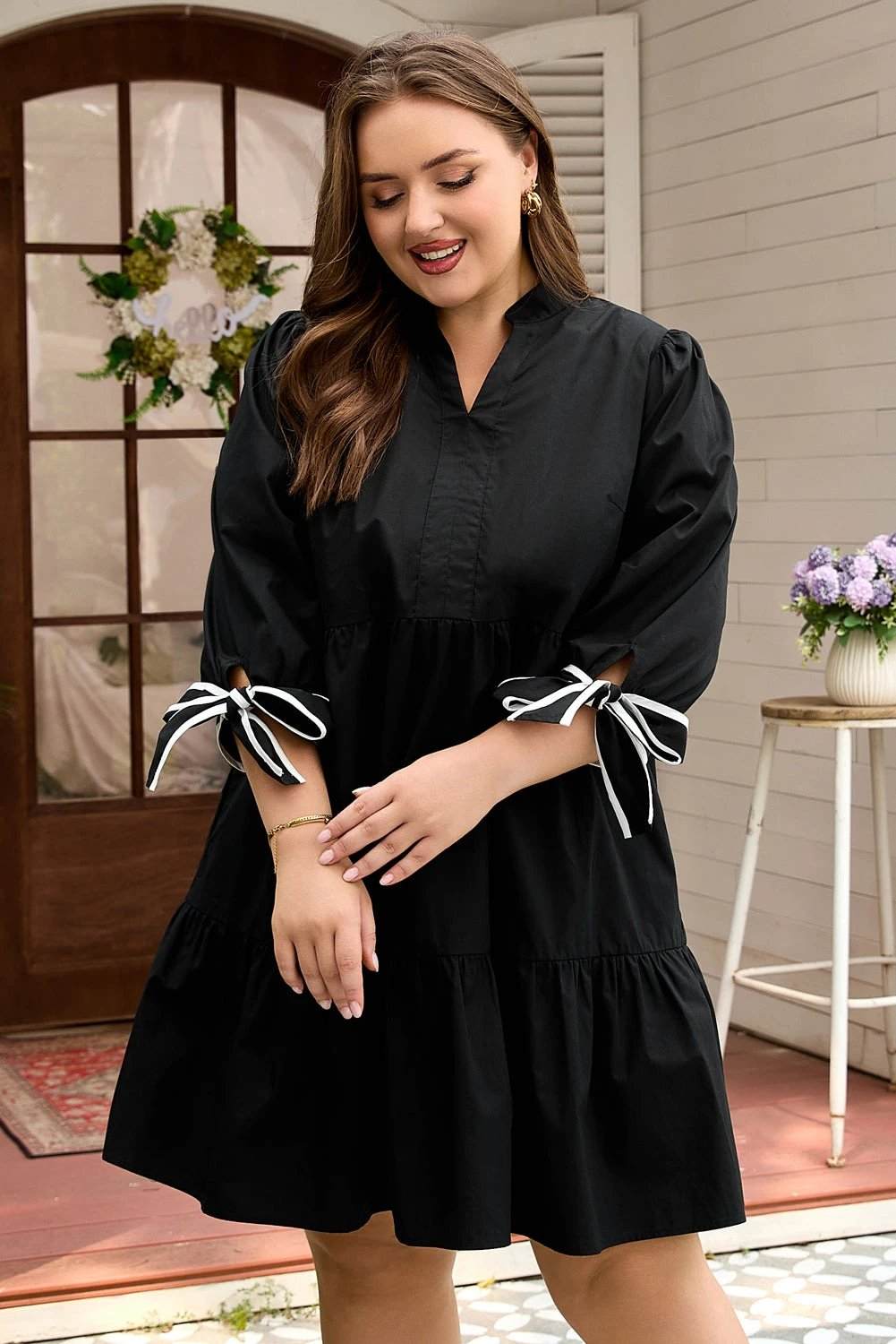 Plus size black V-neck mini dress with contrast trim and knot cuffs on model