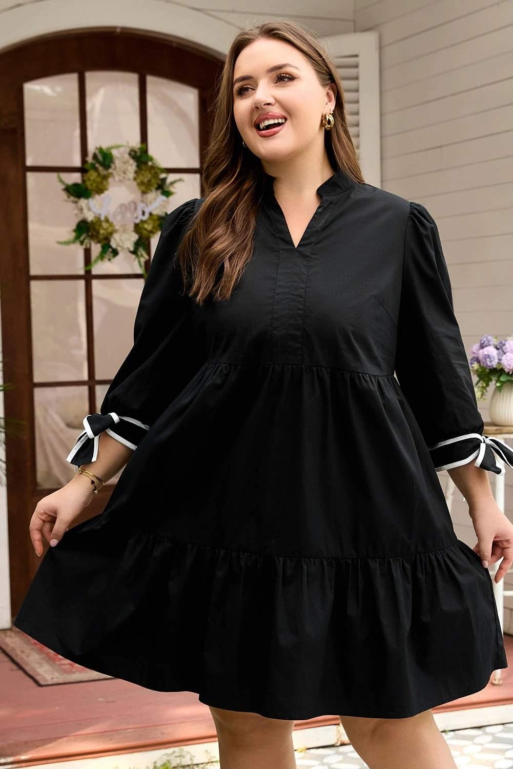 Plus size black V-neck mini dress with contrast trim and knot cuffs on model