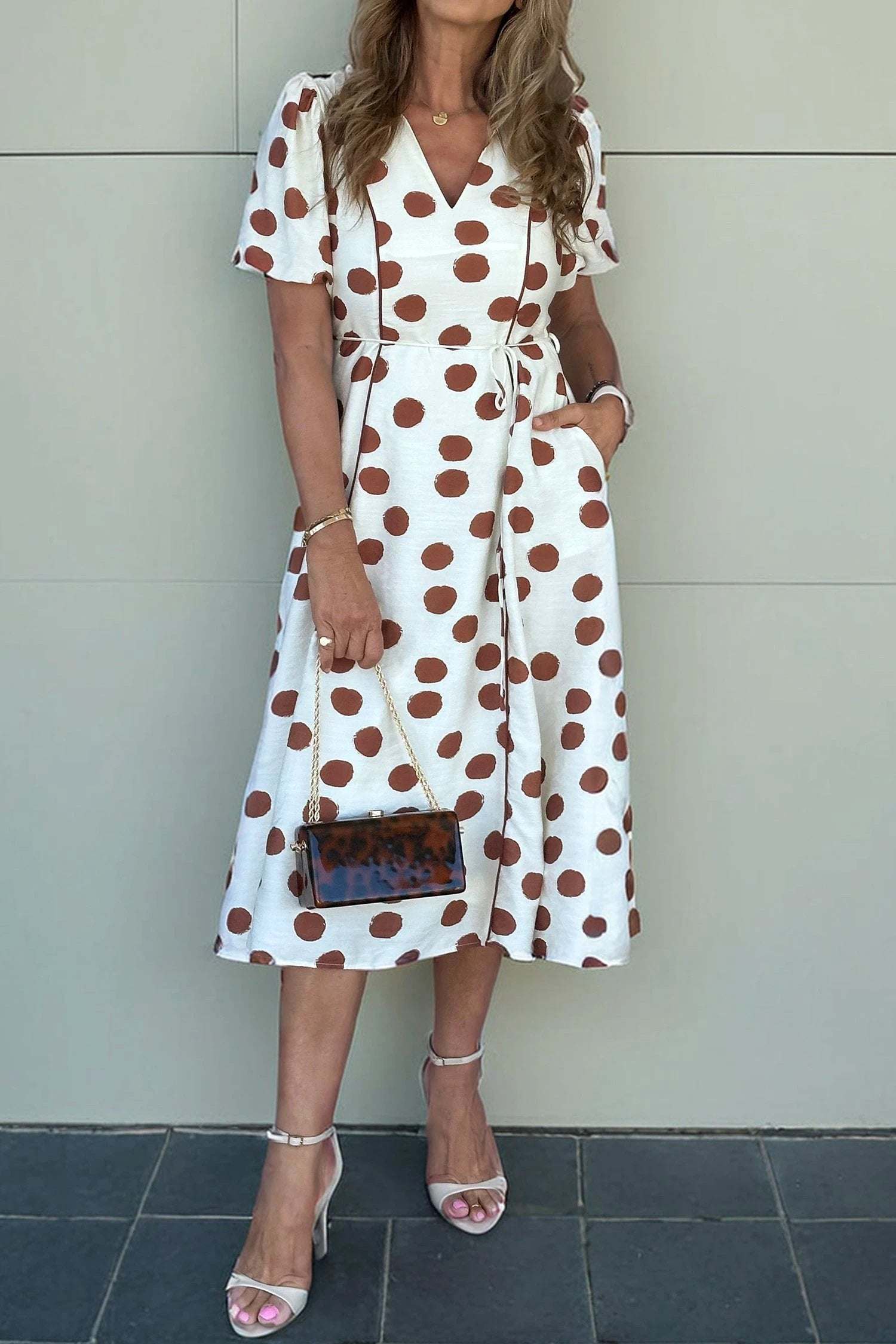 Woman wearing Polka Dot Daydream midi dress with V-neck, tie waist, and brown polka dots on white fabric