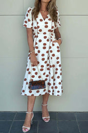 Woman wearing Polka Dot Daydream midi dress with V-neck, tie waist, and brown polka dots on white fabric