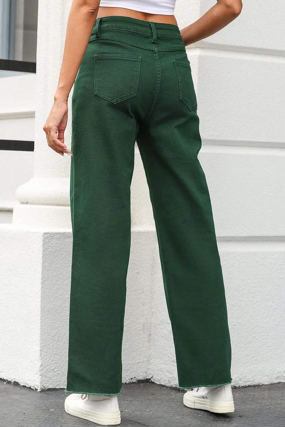 Woman wearing crossed waist raw-hem jeans with a relaxed straight-leg drape.
