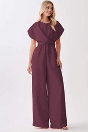 Woman wearing a wine-colored knot-waist cap sleeve jumpsuit with wide-leg silhouette