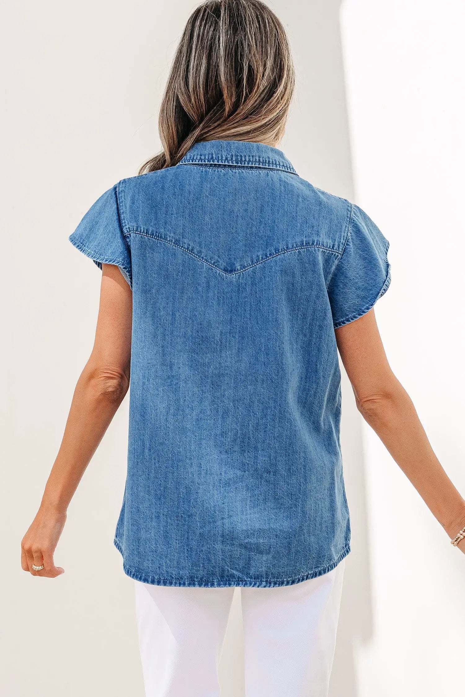 Woman wearing denim ruffled short sleeve shirt with button front and flutter sleeves