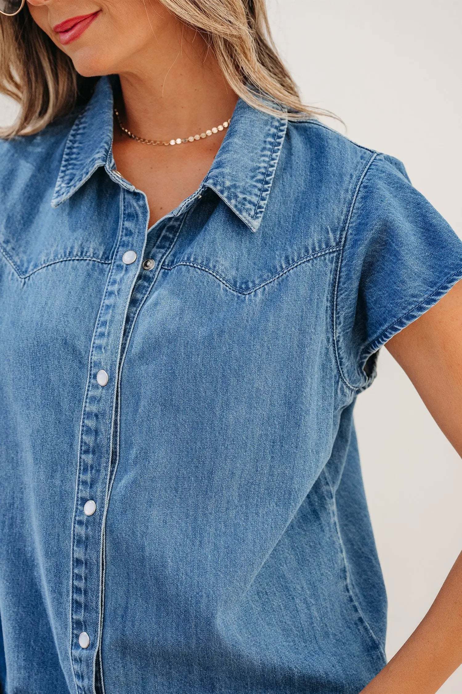 Woman wearing denim ruffled short sleeve shirt with button front in relaxed fit