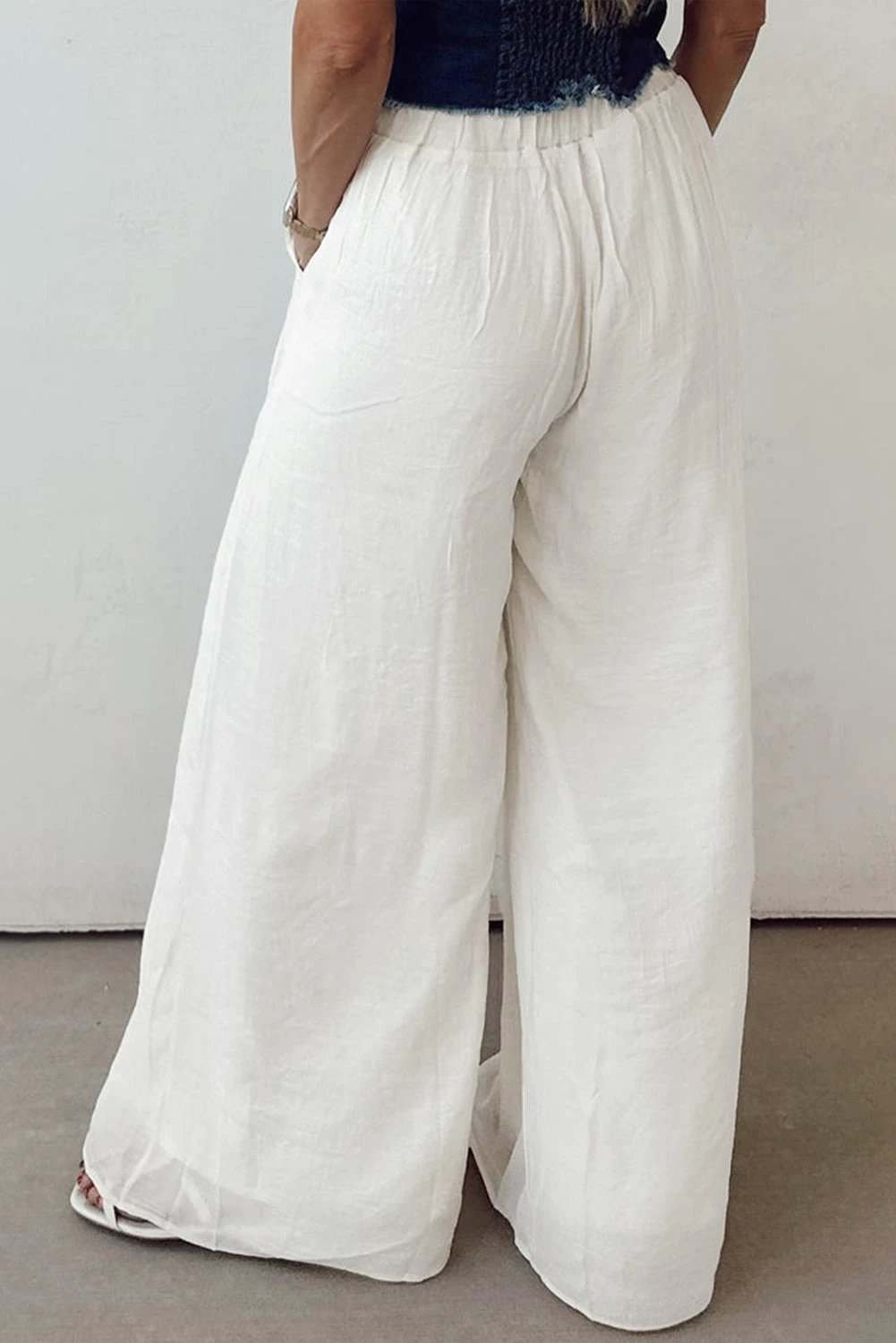 Woman wearing white drop-waist pleated wide-leg cotton-linen pants standing outdoors