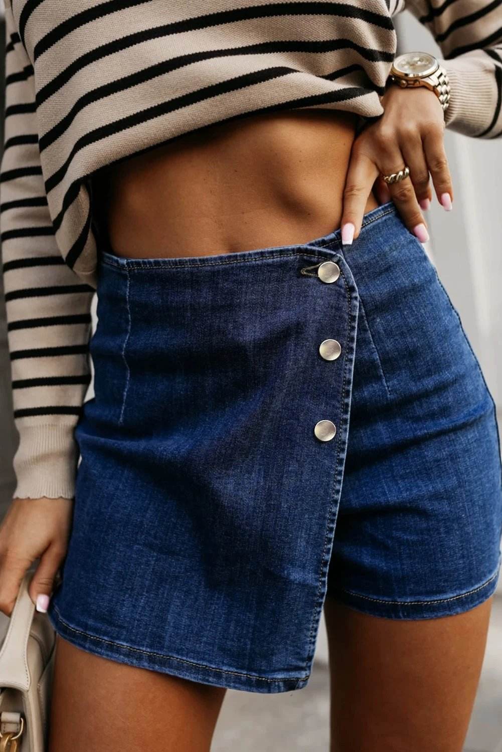 Asymmetric wrapped button-front high waist denim shorts with metallic buttons and stretch fabric