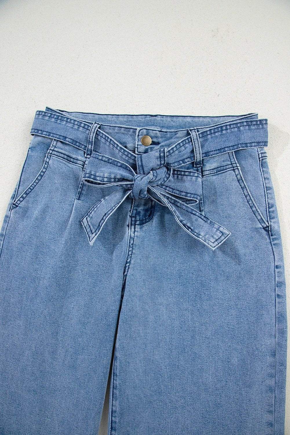 Woman wearing acid washed bow knot sash wide leg jeans standing outdoors on sidewalk