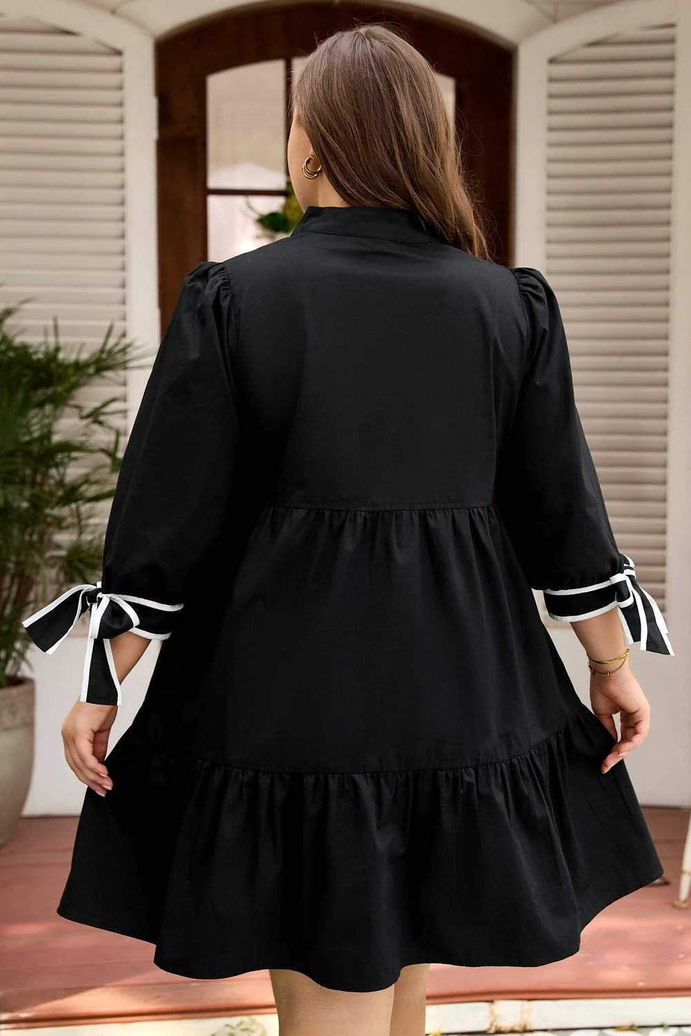 Plus size black V-neck mini dress with contrast trim and knot cuffs on a model