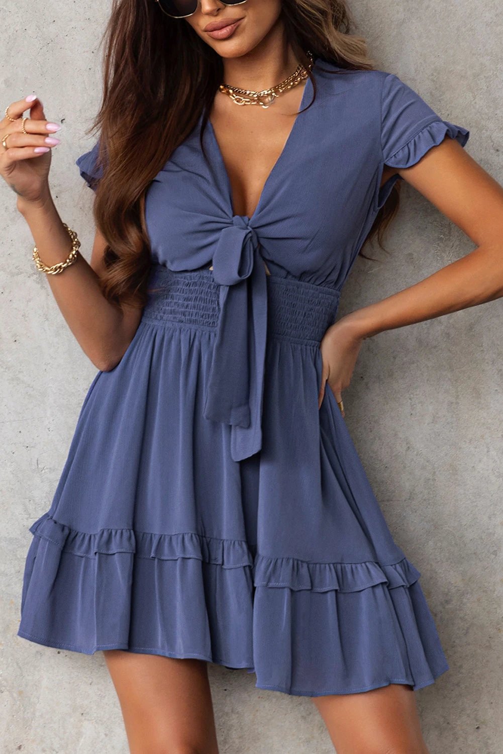 Woman wearing a blue deep V neck dress with self-tie knot and layered flare mini skirt