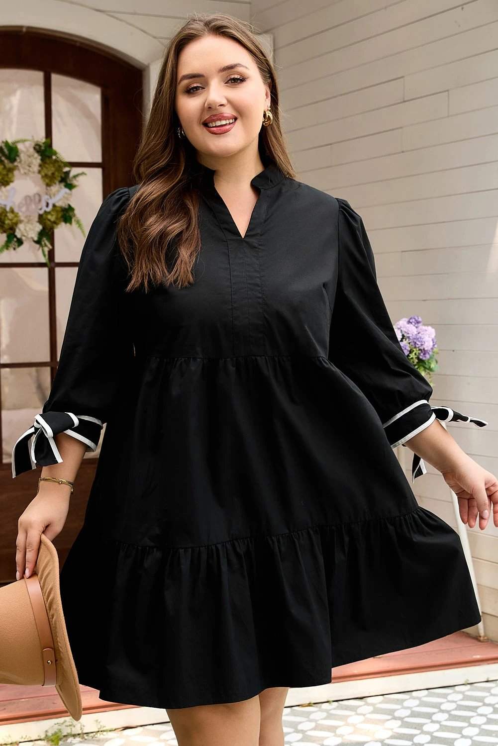 Plus size black V-neck mini dress with contrast trim and knot cuffs on a model