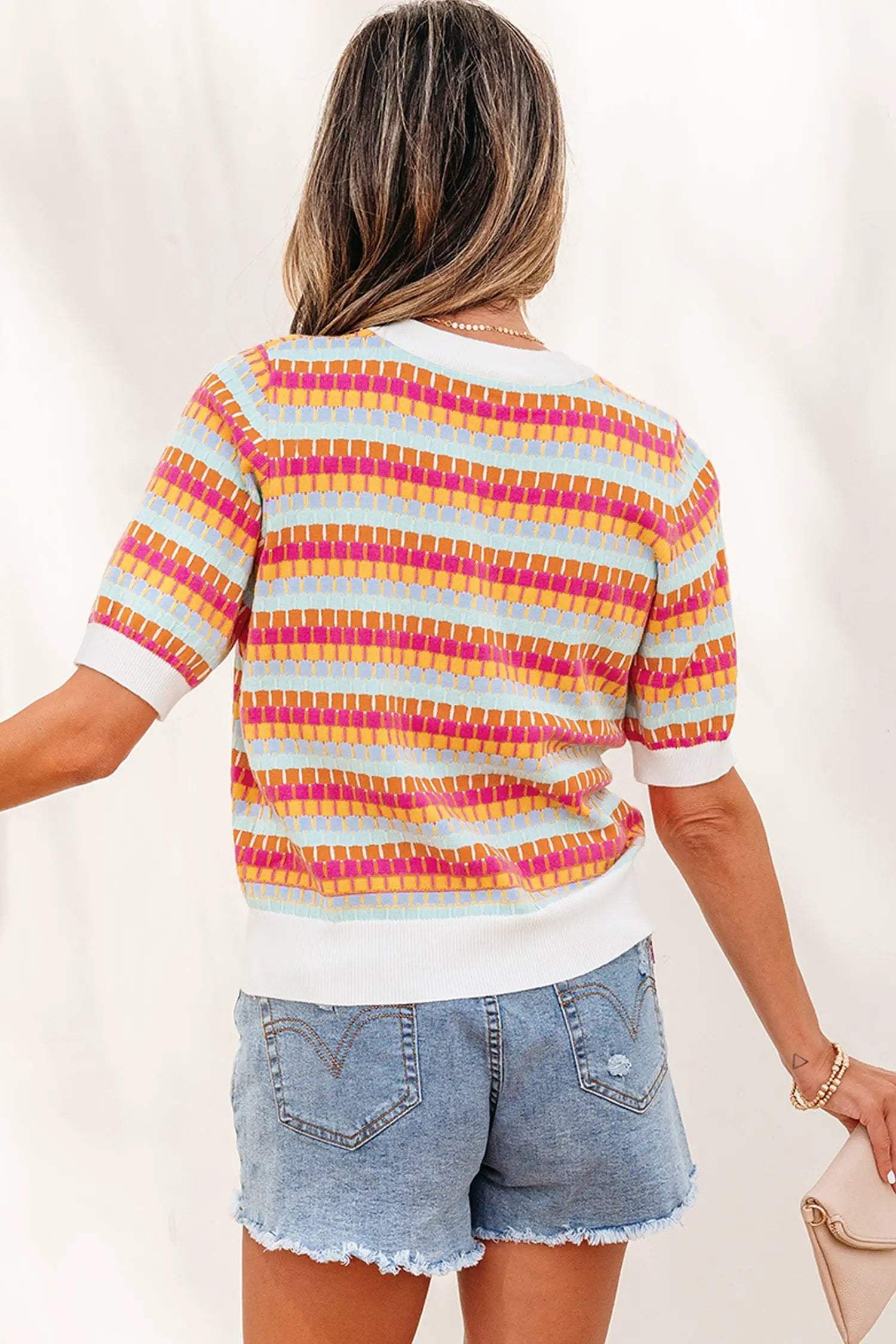 Woman wearing vibrant orange striped knit sweater with short sleeves and abstract stripes