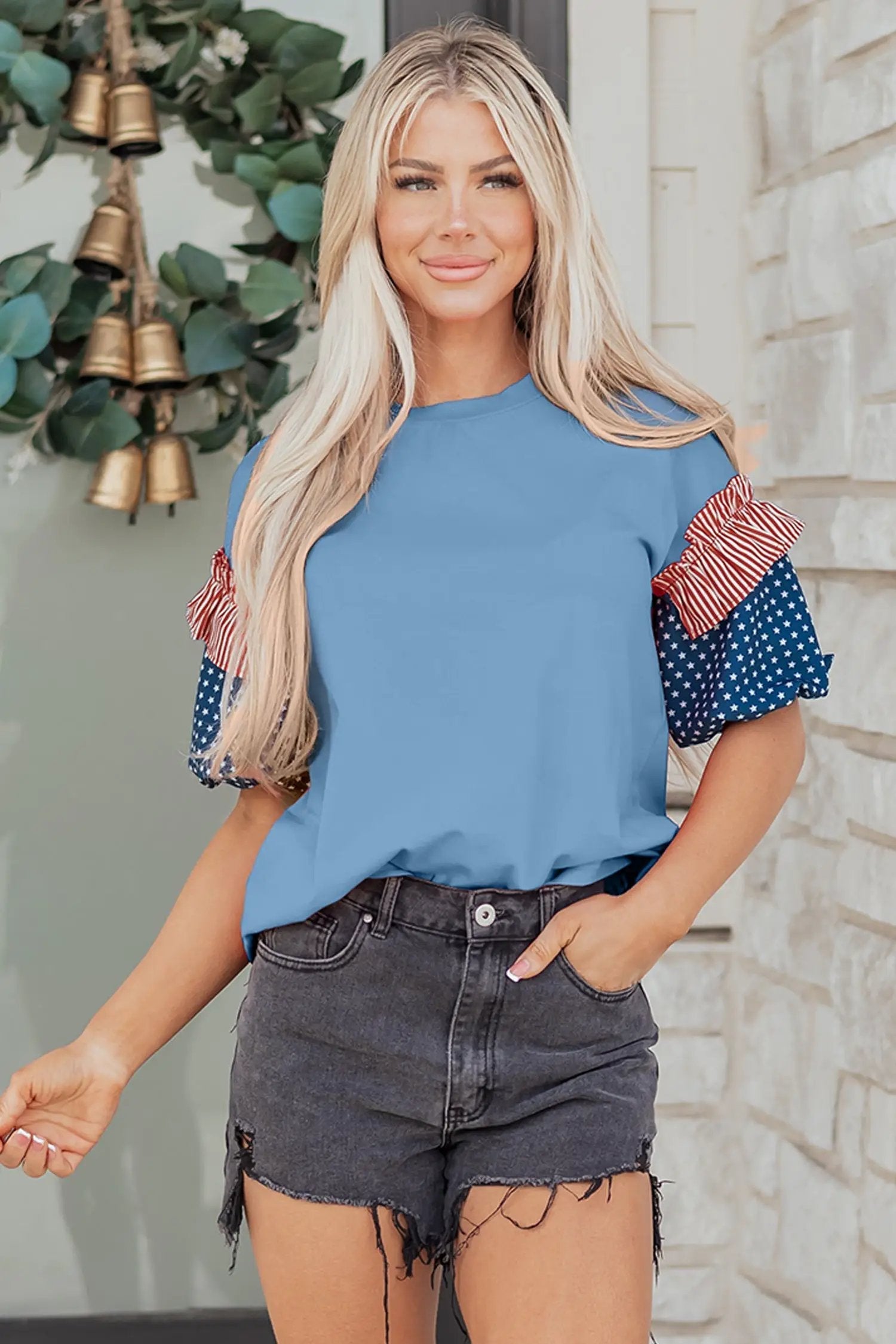 Woman wearing a patriotic puff sleeve top with fiery red stars stripes and American flag print on sky-blue fabric