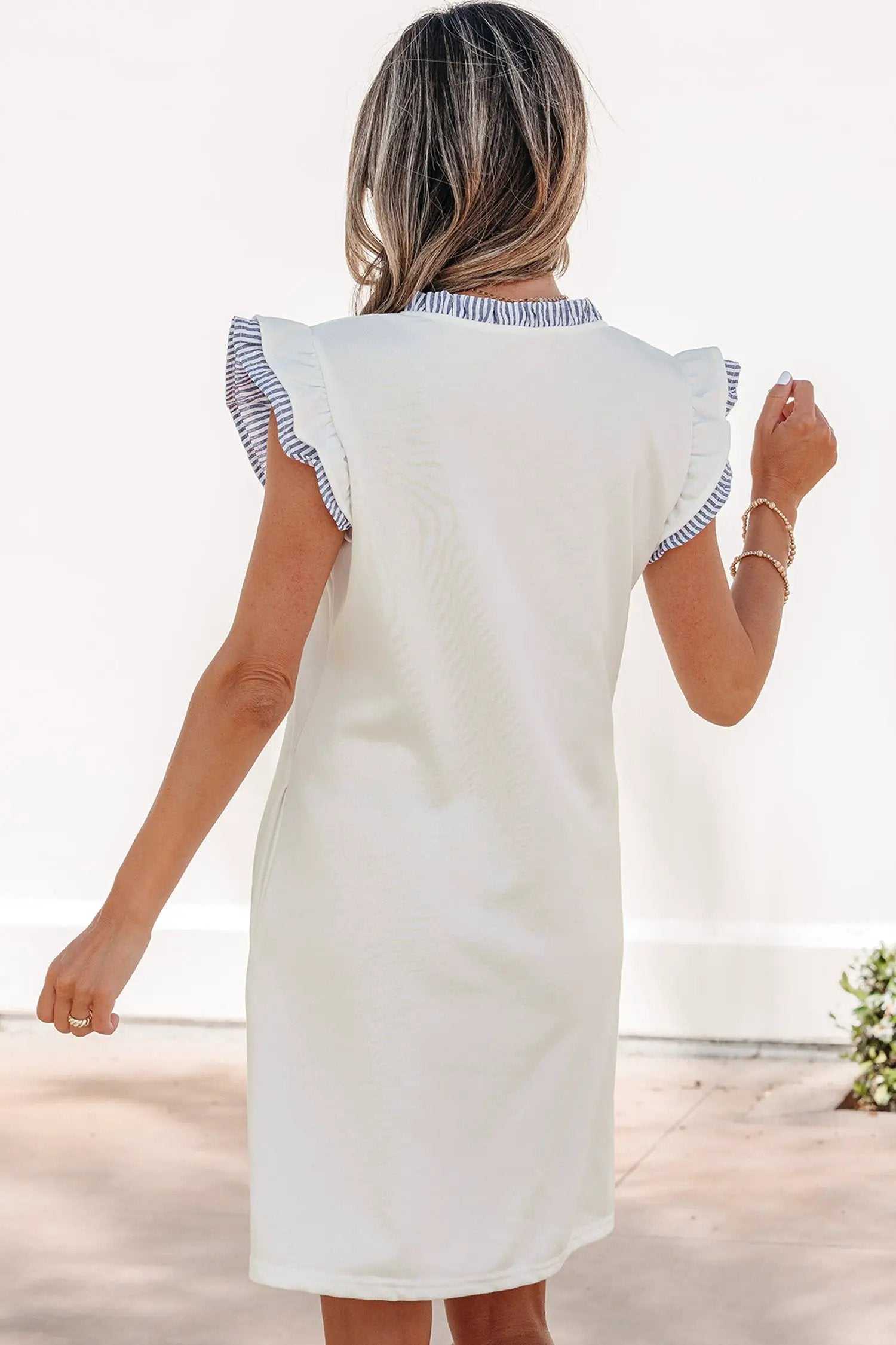 Woman wearing a striped sleeveless dress with split neck and ruffle trim outdoors