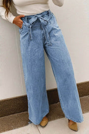 Woman wearing acid washed bow knot sash wide leg jeans standing outdoors with hands on hips