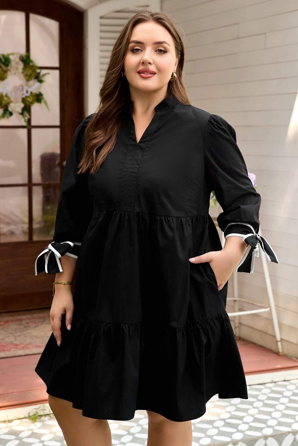 Plus size black V-neck mini dress with contrast trim and knot cuffs on model
