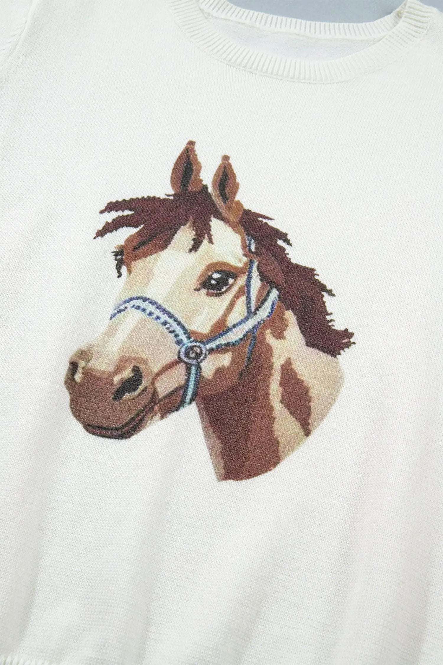 White sweater with a horse head design on a plain background